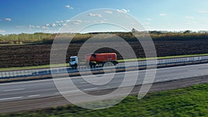 The tanker passes through the countryside. The semi truck with an orange-colored tank carries liquid fuel