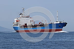 Tanker ship moving in sea full speed ahead. Sunny day, calm blue sea, blue sky.