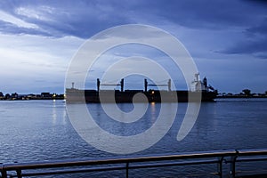 A tanker ship sailing along the flowing waters of the Mississippi River at sunset with blue sky and powerful clouds in New Orleans