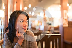 Tanned Asian girl thinking and looking upward to copy space, wondering menu to order for dinner, restaurant advertising concept