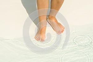 Tanned baby legs enter the water in shallow water in a children`s pool.