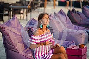 Tanned beautiful woman resting on the beach sofas and drinking a cocktail. Girl smiles and enjoys the sun. Spa and relax concept