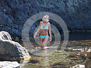 Tanned blond haired female person resting at secluded place of wild rocky seashore