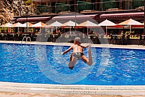 Tanned boy jumps with a run in the outdoor summer pool , rear view
