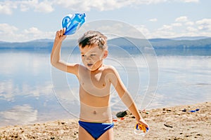 Tanned boy of three years in swimming trunks plays on the lake in the summer, childhood