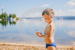 Tanned boy of three years in swimming trunks plays on the lake in the summer, summer vacation, childhood