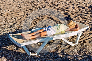 Tanned child lies covered with a hat on a sunbed on the sand