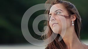 Tanned face of a charming young girl with long hair, which sensually poses on the camera in the evening on the coast