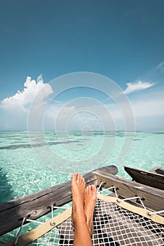 Tanned feet of a woman relaxing on a hammock on the ocean
