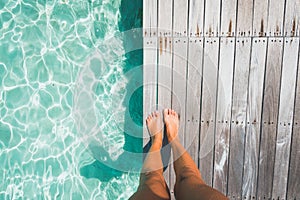 Tanned feet of a woman standing on a wooden deck by tropical ocean