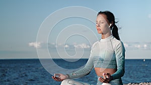 Tanned fitness woman practicing yoga meditating with closed eyes on sunset beach sea sky coast