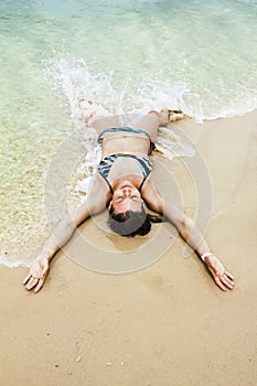 Tanned girl in bikini luxuriating in the waves on the beach
