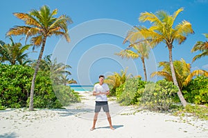 Tanned handsome man wearing white t-shirt and black shorts standing at tropical sandy beach at island luxury resort