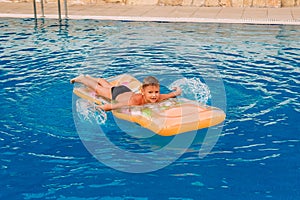 Tanned and happy boy floating on an inflatable mattress in an outdoor pool