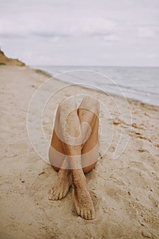 Tanned legs of a girl on beach with sand on smooth skin. Beautiful authentic and unusual image. Young woman relaxing on seashore