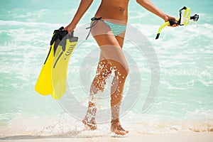 Tanned legs of girl with fins and mask near sea
