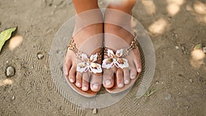 Tanned legs of a little girl in slates with a decorative butterfly. Girl barefoot in summer shoes on sand. Philippines.