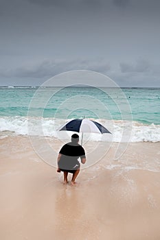 Tanned man jump with umbrella in blue sea