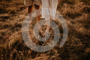 tanned man and light skin legs woman barefoot close-up walking on dry green thin grass.