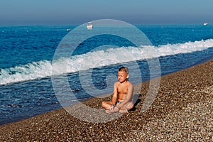 Tanned nine-year-old boy in bathing fits sits back on the pebble shore of the sea photo