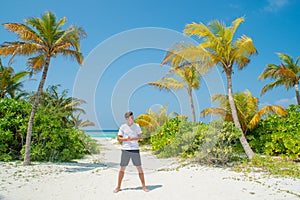 Tanned tall handsome man wearing white t-shirt and black shorts standing at tropical sandy beach at island luxury resort