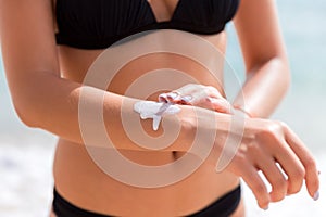 Tanned woman is applying sunscreen on her hand at the beach