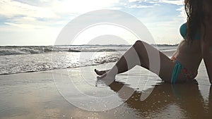 Tanned woman in swimsuit relaxes on ocean shore and admires beautiful landscape. Young girl in bikini sits on the coast