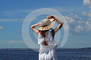 Tanned woman in white dress and hat on riverside