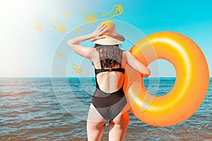 Tanned young woman holding an orange inflatable circle and holding her head. The sea in the background. The concept of summer