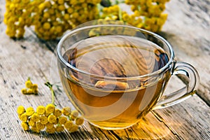 Tansy infusion in a glass cup on a wooden table. Tansy Herbal tea. Healing herbs