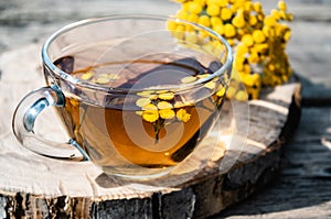 Tansy infusion in a glass cup on a wooden table. Tansy Herbal tea. Healing herbs