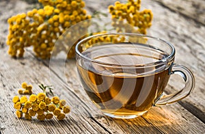 Tansy infusion in a glass cup on a wooden table. Tansy Herbal tea. Healing herbs