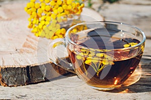 Tansy infusion in a glass cup on a wooden table. Tansy Herbal tea. Healing herbs