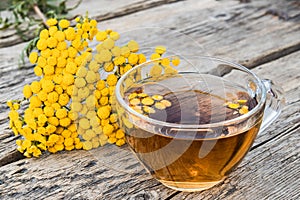 Tansy infusion in a glass cup on a wooden table. Tansy Herbal tea. Healing herbs