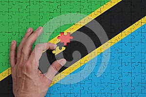Tanzania flag is depicted on a puzzle, which the man`s hand completes to fold