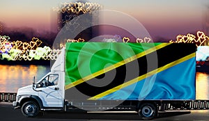 Tanzania flag on the side of a white van against the backdrop of a blurred city and river. Logistics concept