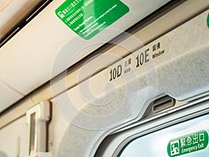 Closeup overhead seat numbers in Taiwan High Speed Rail THSR and Emergency Exit sign with yellow sunlight through the window.