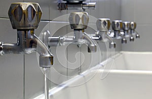 Tap with water and many taps shut and a white ceramic washbasin