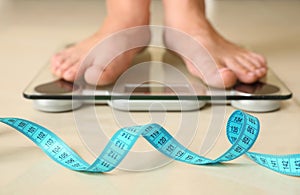 Tape in front of woman standing on floor scales indoors