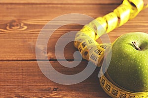 Tape measure and green apple on a wood background top view. The concept of a healthy diet, body weight control, down