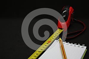 Tape measure pencil and notepad on a dark background