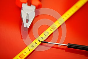 A tape measure, a screwdriver-tap and pliers lie on a red polished surface in a car repair shop. Performance of work