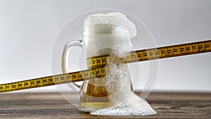 Tape measure wrapped around a glass of fresh draught beer. Diet weight loss concept bad habit beer belly obesity alcohol addict