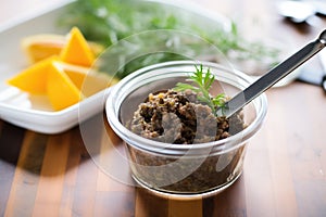 tapenade in a clear container with spreader knife