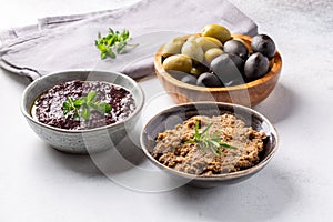 Tapenade - paste made from olives. Bowls with spreadable black and green olive cream on concrete background