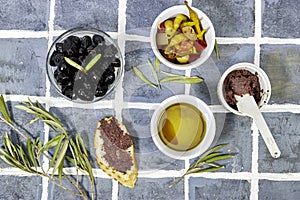 Tapenade - paste made from olives. Bowls with spreadable black and green olive cream and oil on tiles background,