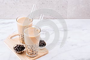 Tapioca pearl ball bubble milk tea, popular Taiwan drink, in drinking glass with straw on marble white table and wooden tray,