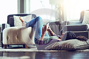 Tapping into the weekend. a young woman using a mobile phone while relaxing on the floor at home.