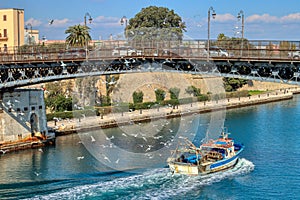 Taranto swing bridge with fishing boat returning to the port surrounded by dozens of seagulls. Puglia, Italy