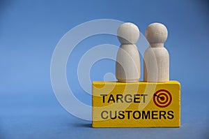 Target customers text on yellow wooden block with model wooden dolls on top. Business and marketing concept